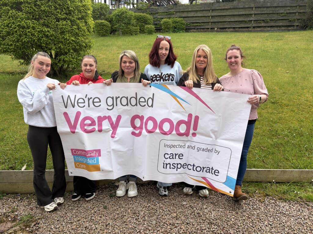 Colleagues are smiling and holding up a banner reading 'We're rated Very Good by the Care Inspectorate'.