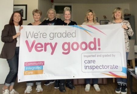 A group of colleagues at Eden Drive Service smiling and facing the camera while holding a banner that reads ‘We’re graded Very Good!’