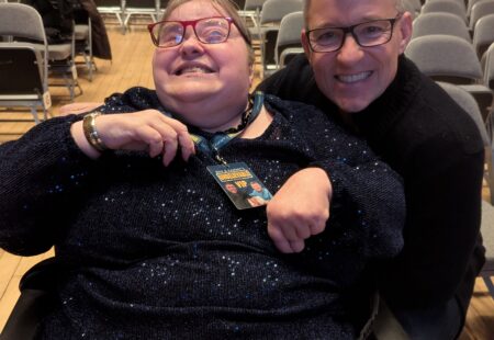 Judith, smiling in her wheelchair, next to TV presenter Ben Shephard at a venue, both looking happy as they smile facing forward at the camera.