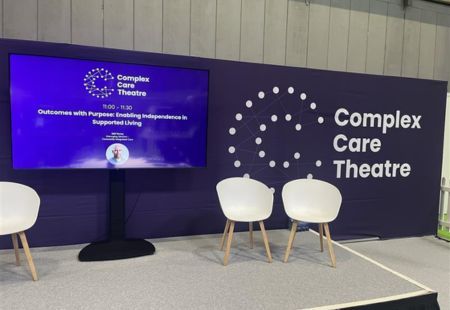 A stage at a the Care Management Show with a big screen in the background. Edd's face in on screen next to his session title.