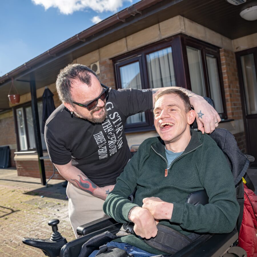 A person we support sat in a wheelchair with their support worker stood beside him