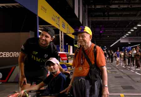 Formula E driver, Jake Dennis, stands smiling to camera with Ayaz and Aaron (people supported by Community Integrated Care). They are at the side of the track at the Formula E in London,