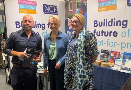 Three people stood in front of an exhibition stand which reads 'Building the Future of Not-for-profit social care'