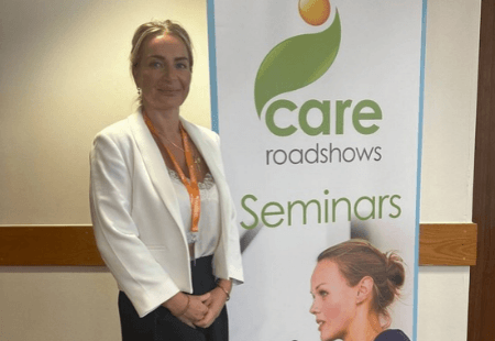Olivea stood smiling to camera in front of a banner that reads 'Care roadshows'